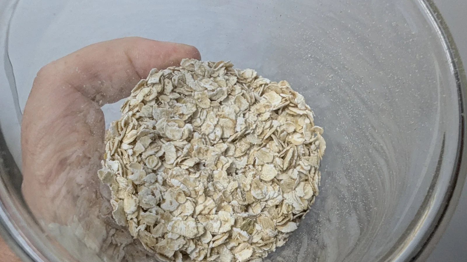 Hand mit einer Portion Haferflocken über einer Glasschüssel