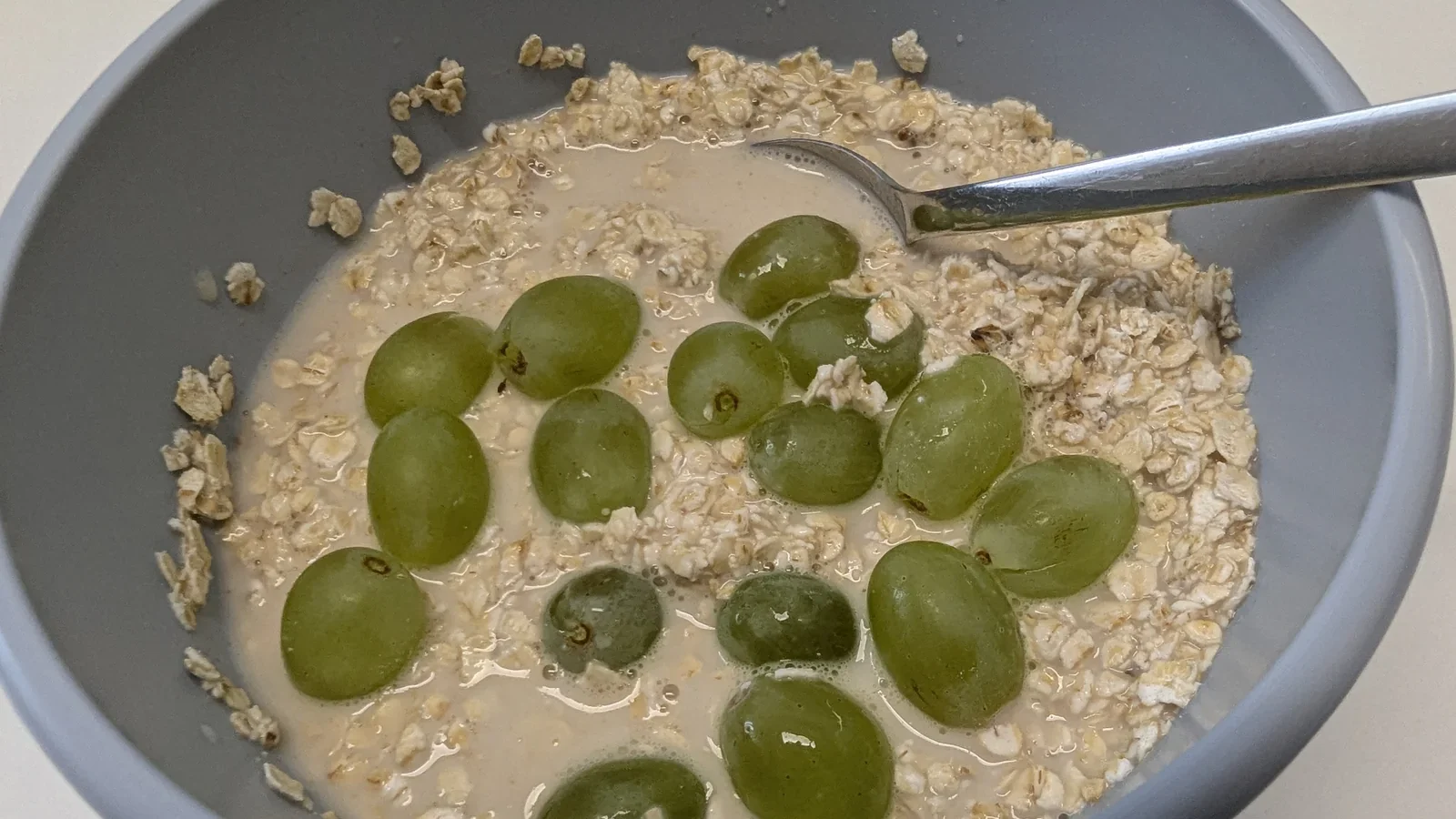 Graue Schale mit eingeweichten Haferflocken und grünen Trauben