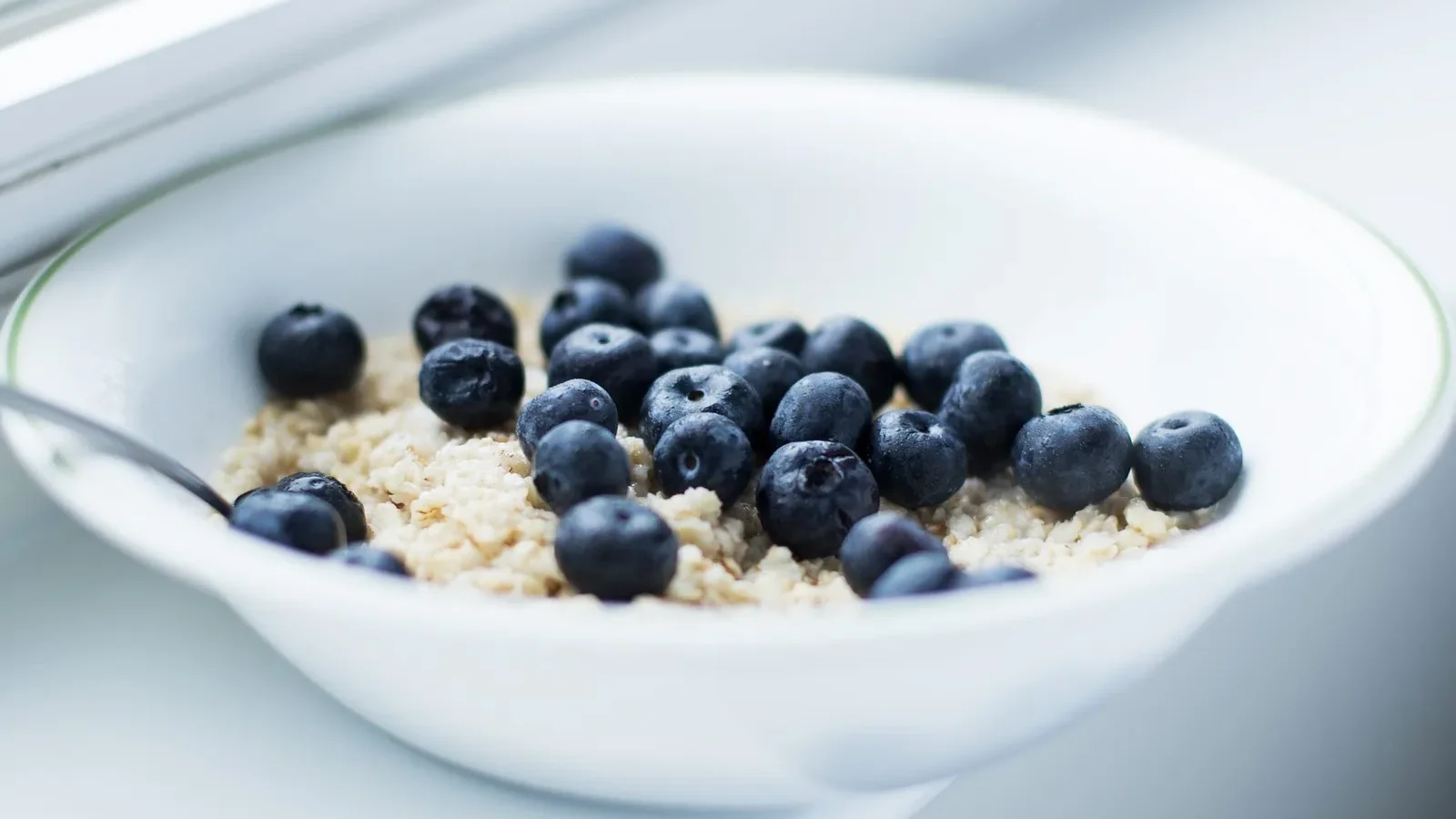Helle Schale Porridge mit Heidelbeeren am Fenster